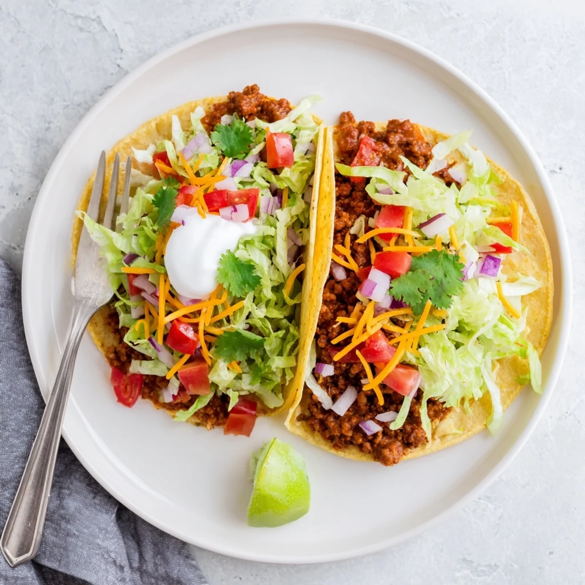 Hearty beef tacos with a zesty homemade seasoning blend, garnished with cilantro, red onion, and a dollop of sour cream on a rustic plate.  