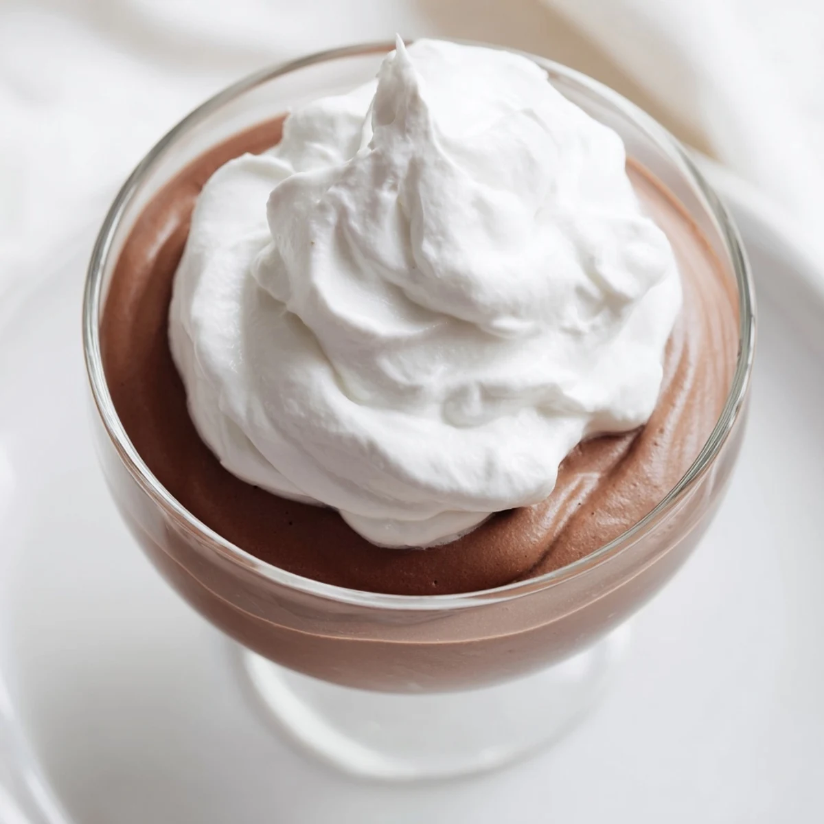 Smooth chocolate mousse with whipped cream, served in a glass with fresh berries on the side.