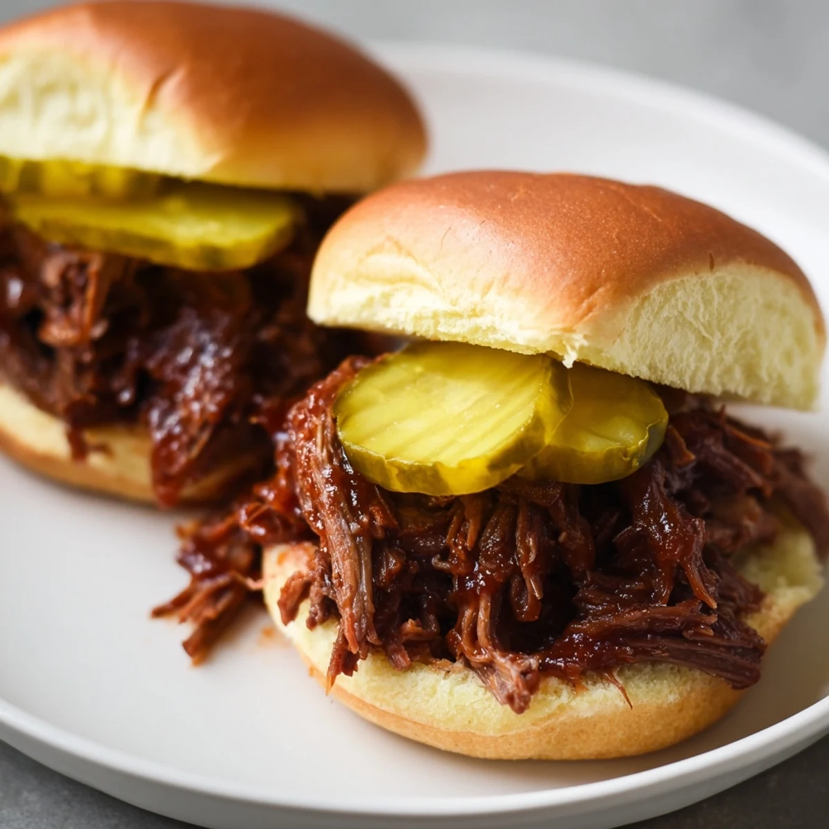 Golden-brown, shredded beef piled high on buttered slider buns, topped with crisp dill pickle slices for a tangy bite.  