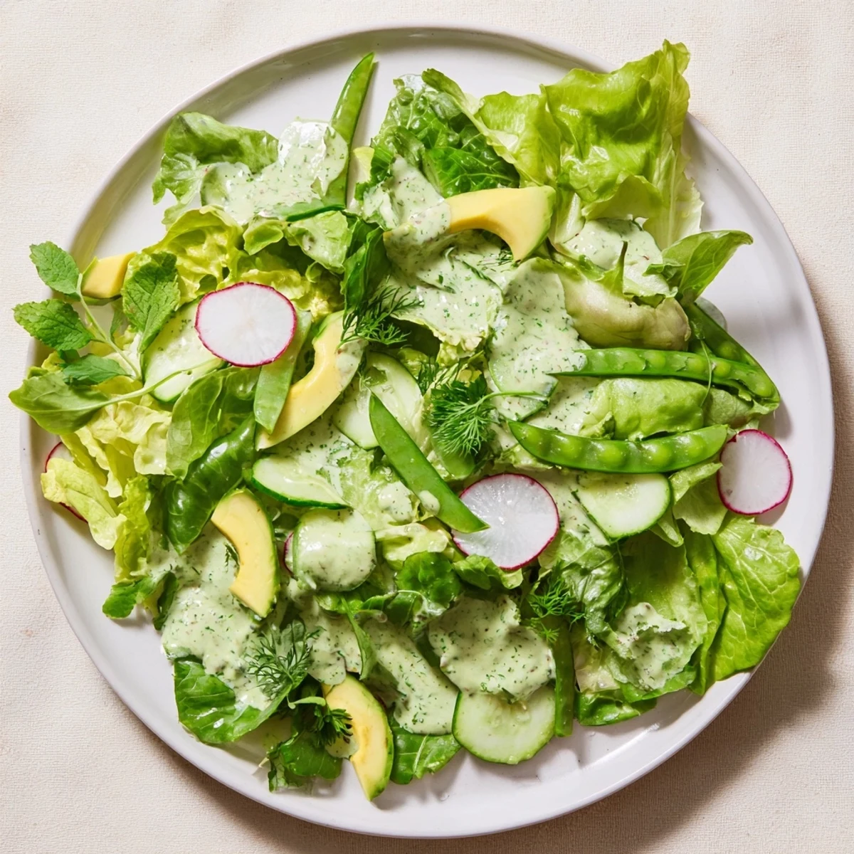 Fresh mixed greens, cucumber, avocado, and radishes tossed in homemade Green Goddess dressing, served in a white bowl.