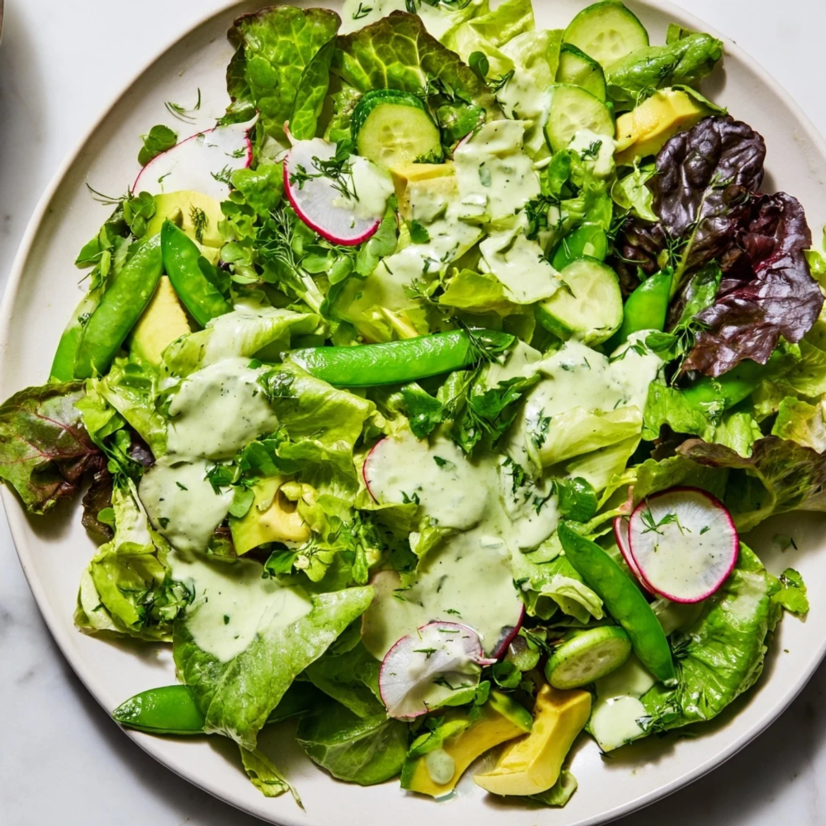 A vibrant bowl of Green Salad with Green Goddess dressing, featuring snap peas and radishes with herbs.
