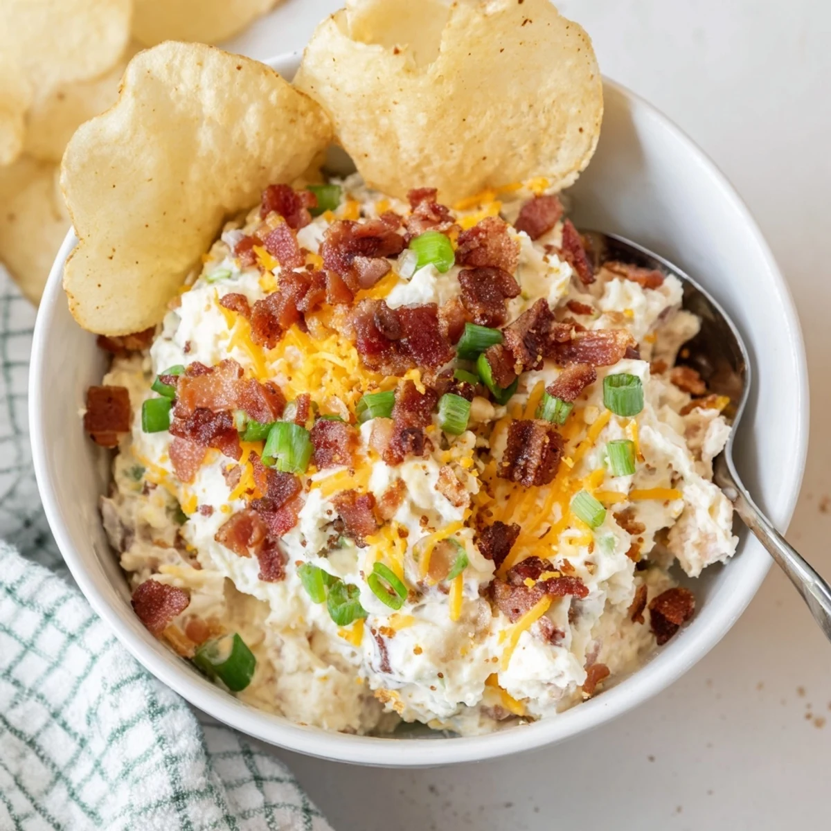Creamy Loaded Baked Potato Dip garnished with bacon and chives served with crispy potato chips for dipping.