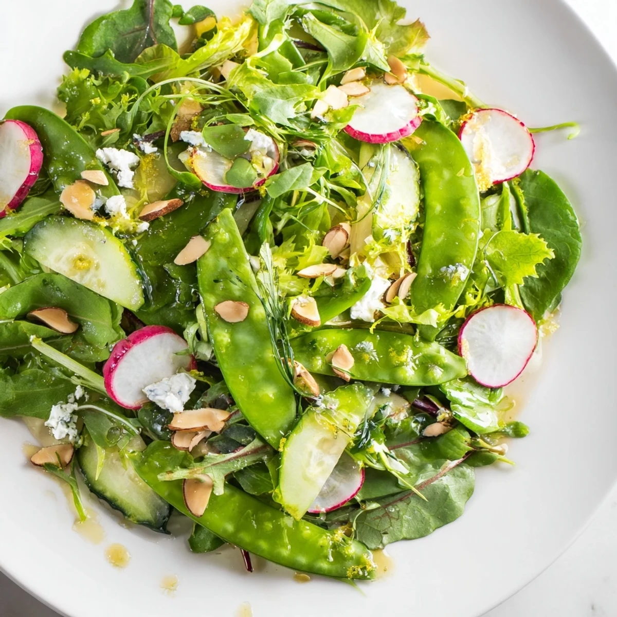 A vibrant bowl of Spring Greens Salad featuring crisp mixed greens, snap peas, and cucumber, lightly dressed with bright lemon vinaigrette.
