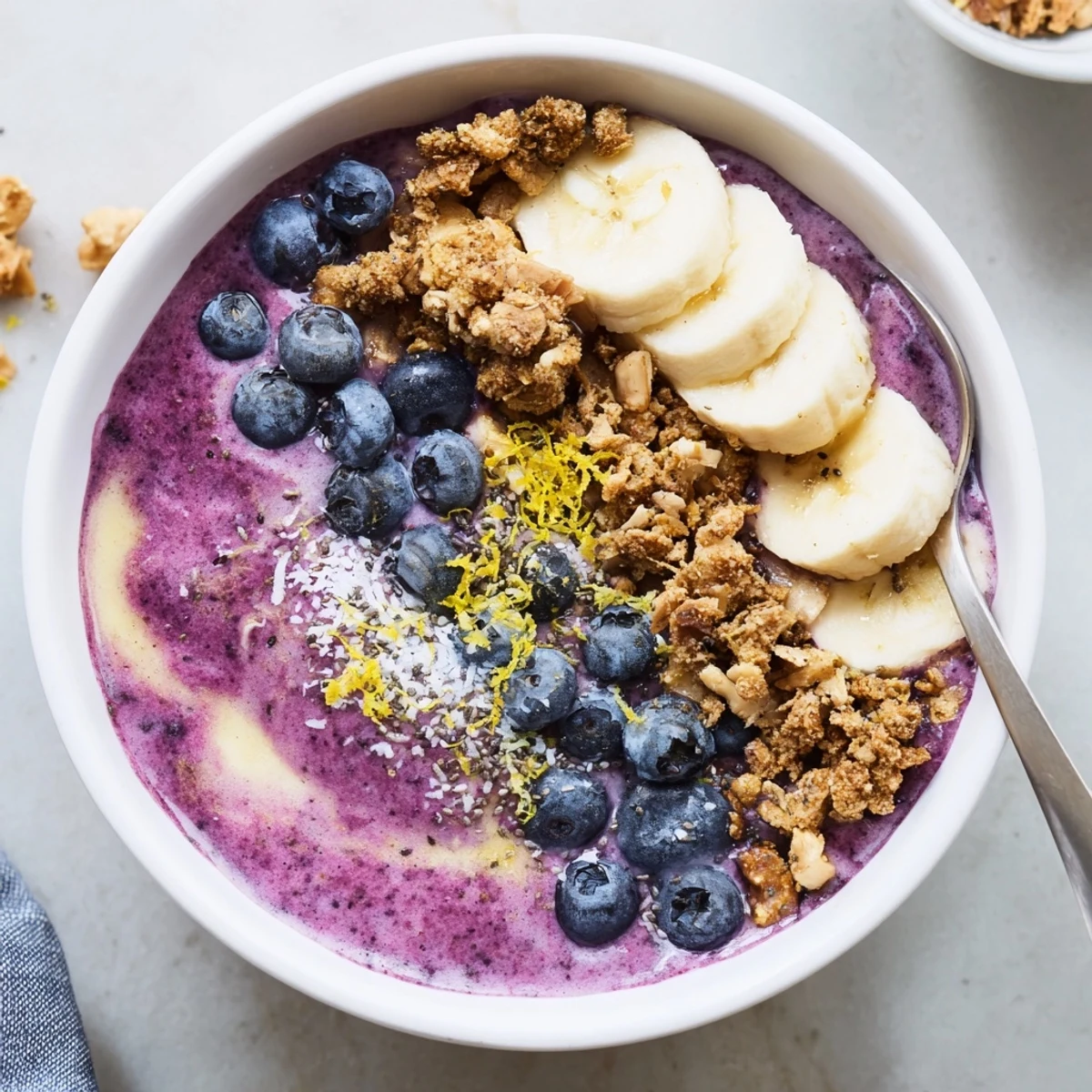 Vibrant Lemon Blueberry Smoothie Bowl topped with crunchy granola and fresh banana slices, served in a chilled bowl. 