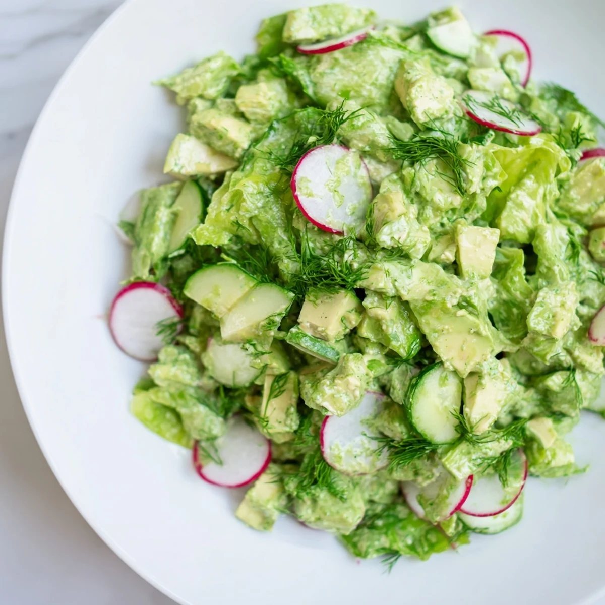 Colorful Green Goddess Salad with avocado and cucumber in a salad bowl with fresh herbs for garnish.