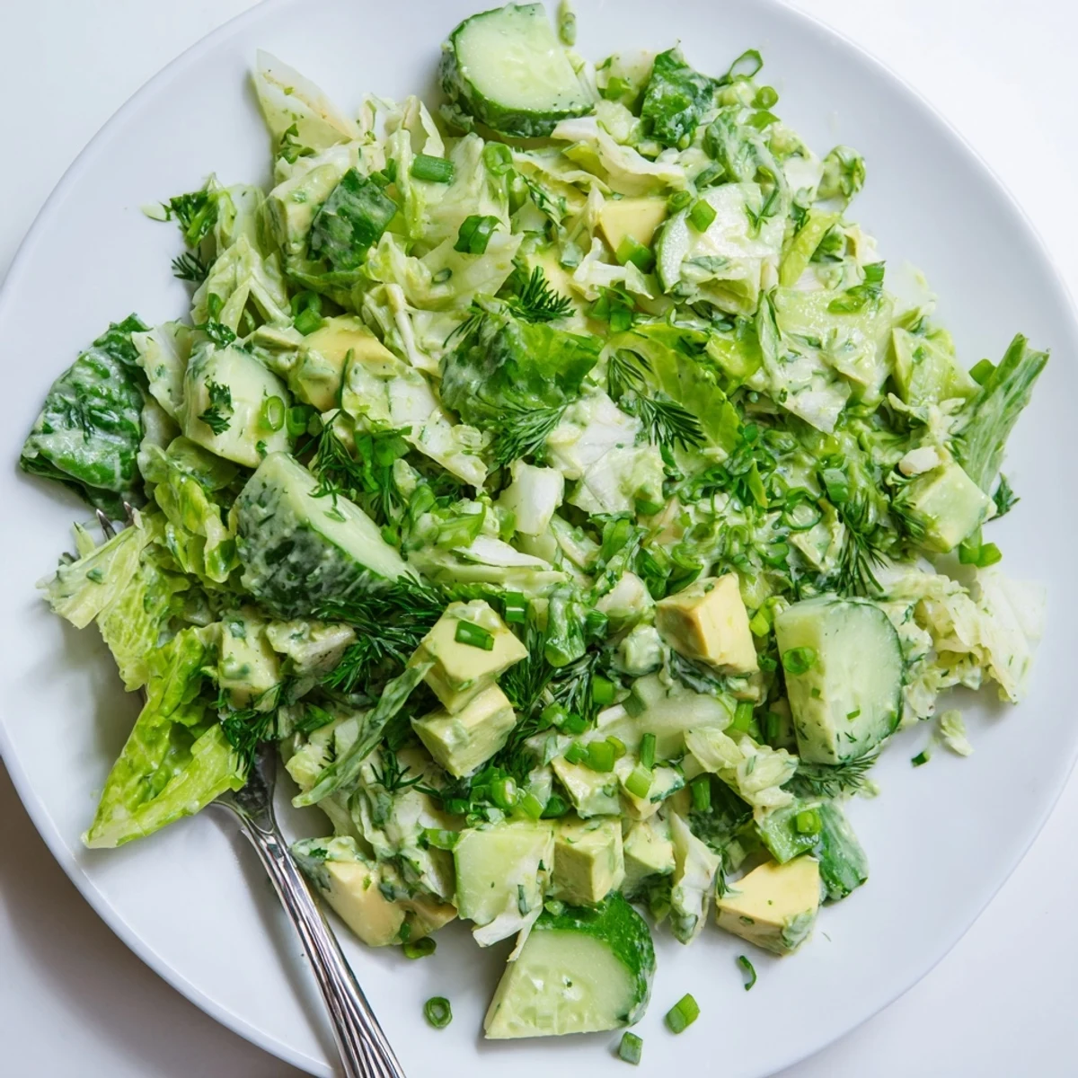 A vibrant Green Goddess Salad with Avocado in a white bowl, featuring crisp romaine and diced avocado tossed in creamy green dressing.