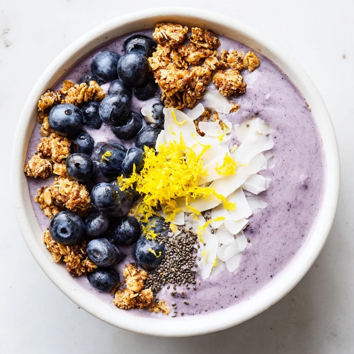 A vibrant Lemon Blueberry Smoothie Bowl with granola, fresh berries, and chia seeds in a white bowl.