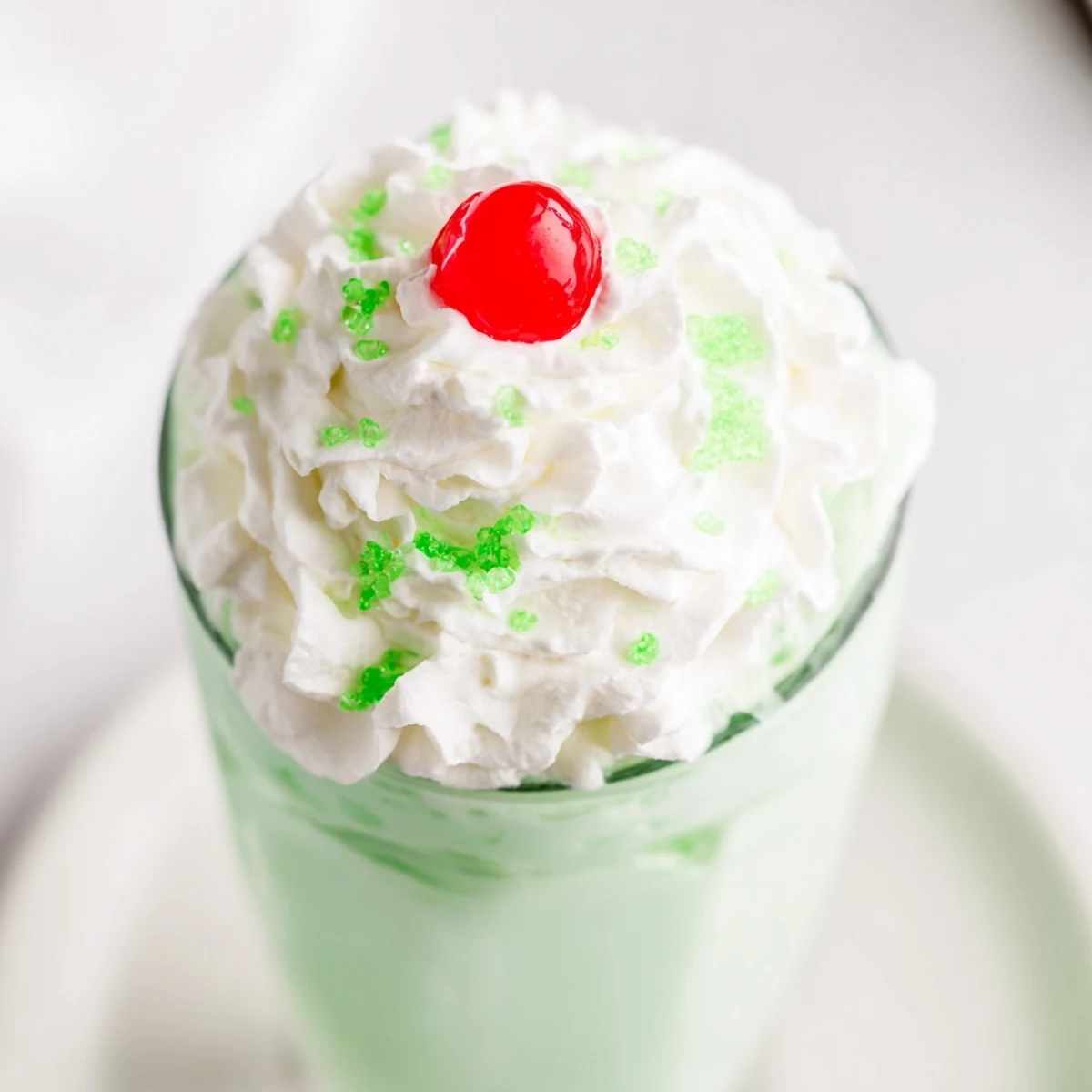 Frothy Homemade Copycat Shamrock Shake in a tall glass beside fresh mint leaves and vanilla ice cream scoops.