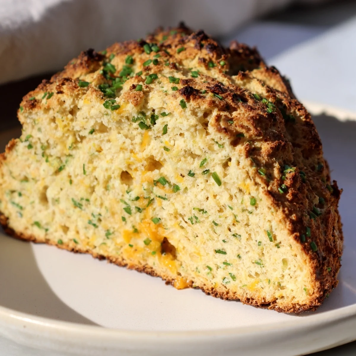 Close-up of a warm Savory Herbed Cheddar Irish Soda Bread loaf, showcasing the craggy crust and cheesy, herbed interior crumb.