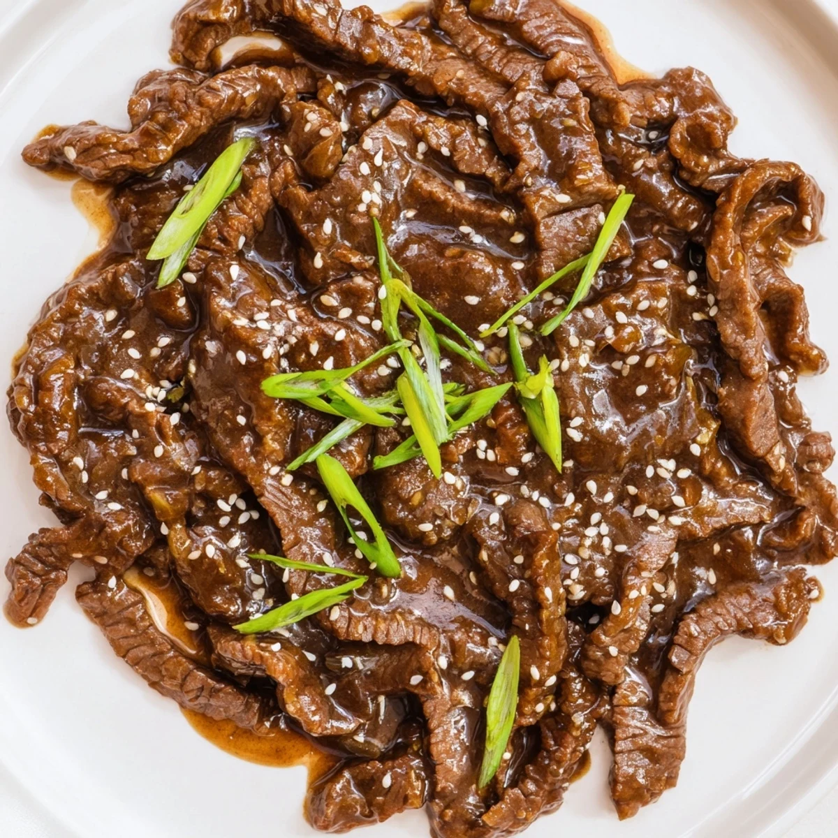 The Ultimate Slow Cooker Mongolian Beef looks tender and saucy, garnished with scallions and sesame.