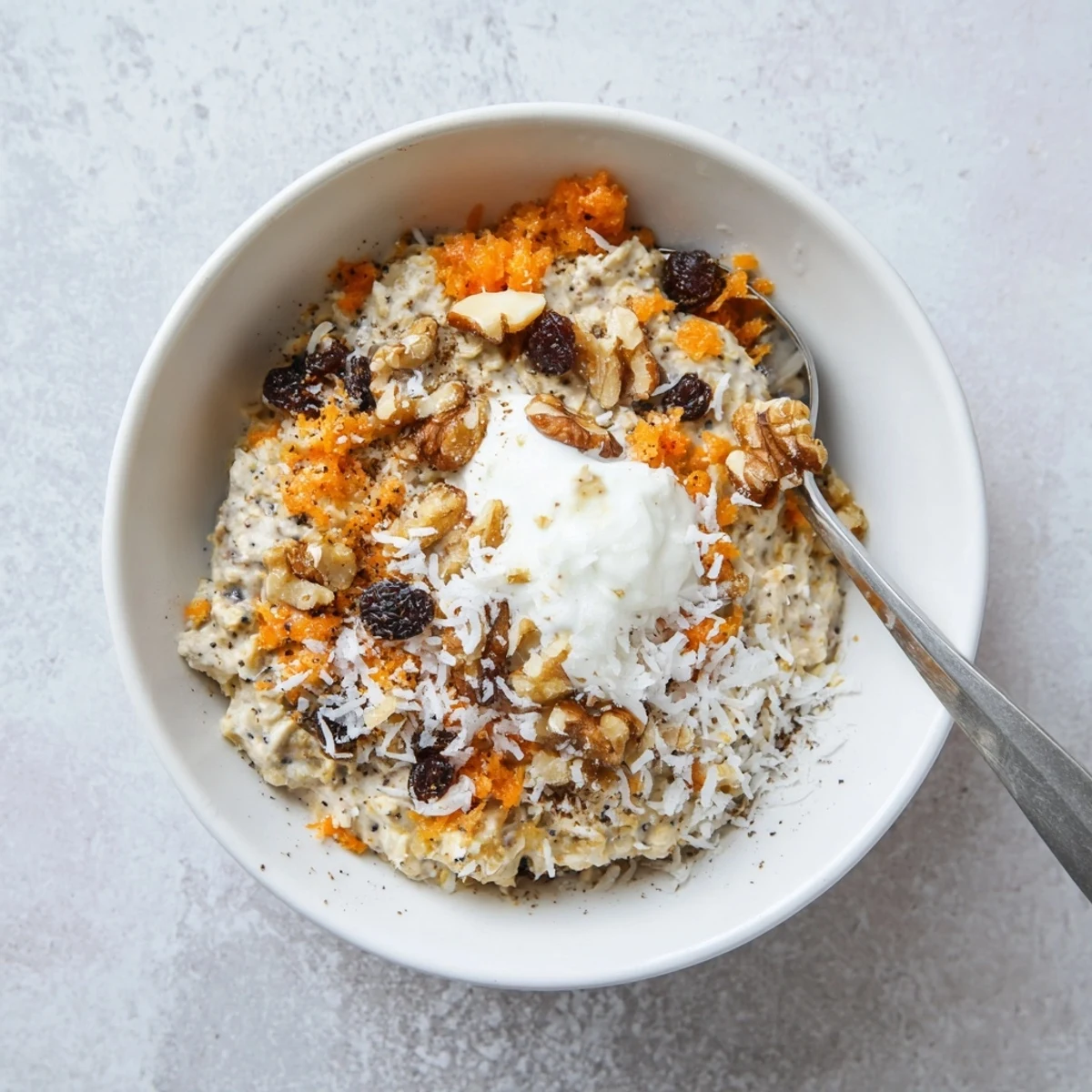 A close-up of chilled Carrot Cake Overnight Oats in a glass jar, topped with chopped walnuts and a drizzle of maple syrup.