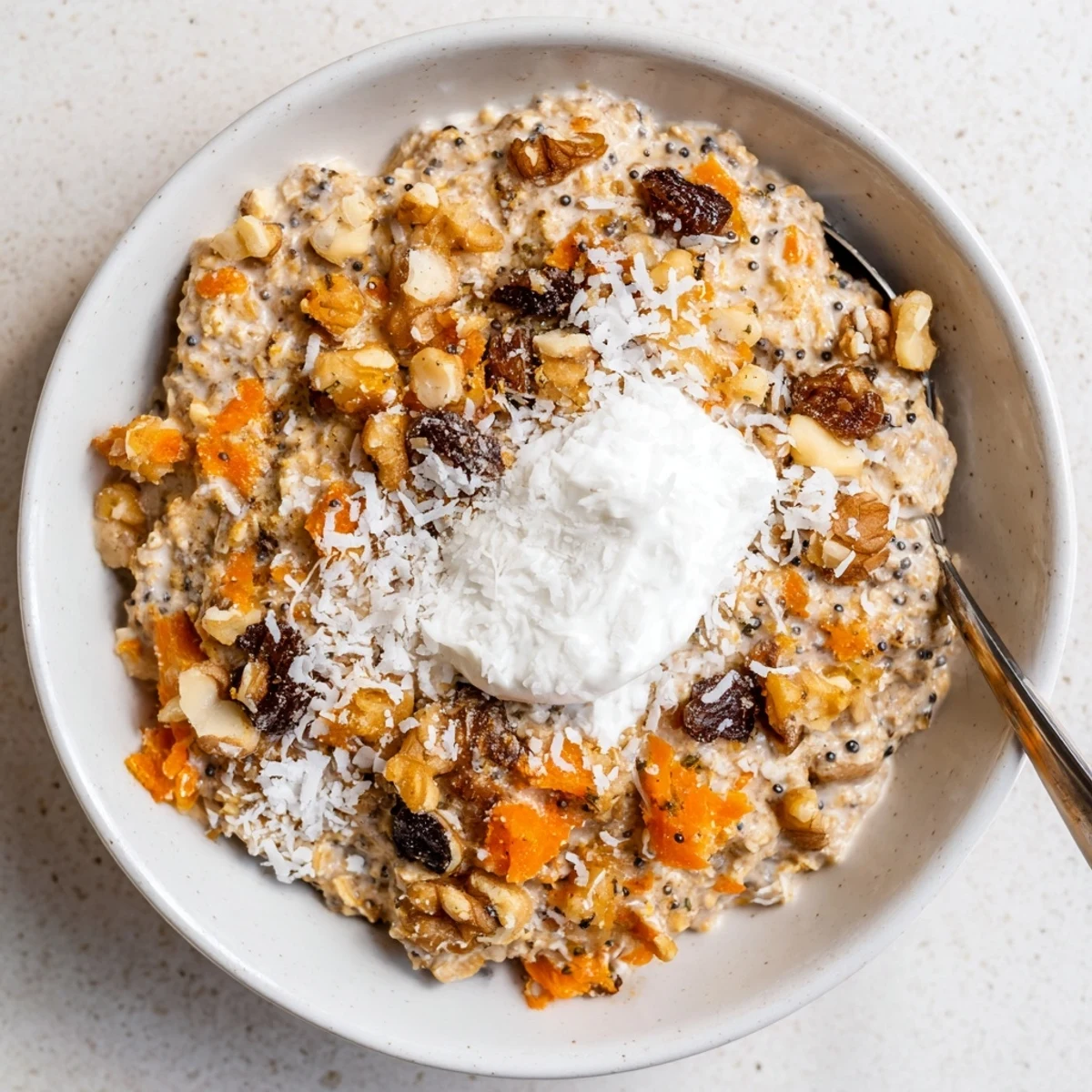 Two clear jars of creamy Carrot Cake Overnight Oats layered with shredded carrots, raisins, and a dollop of Greek yogurt.