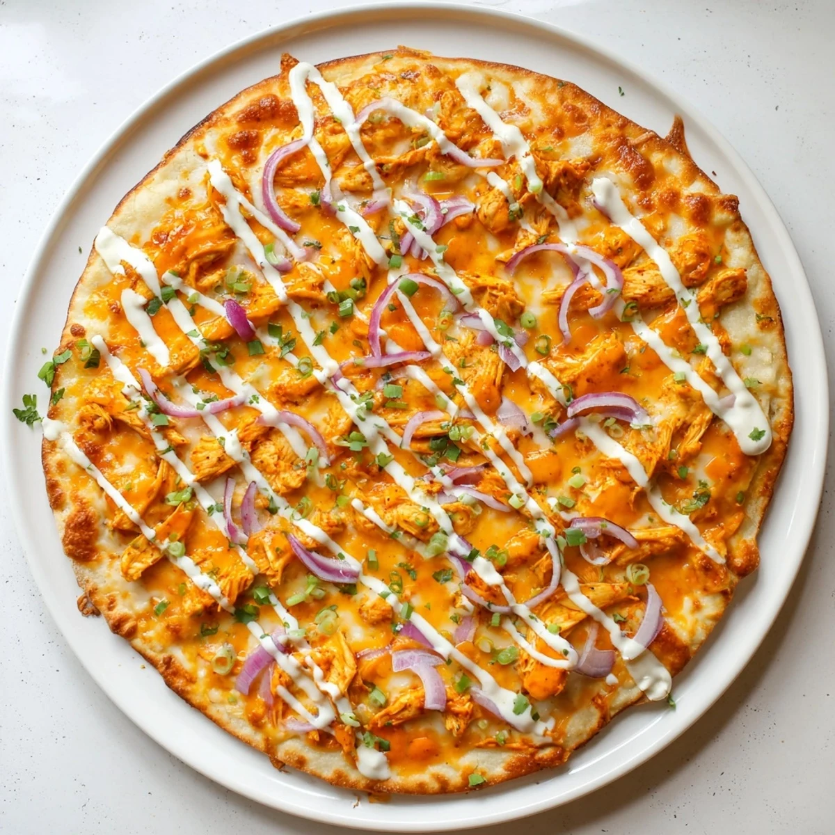 Close-up of Bold Buffalo Chicken Pizza with red onion and scallions, drizzled with ranch and extra buffalo sauce.