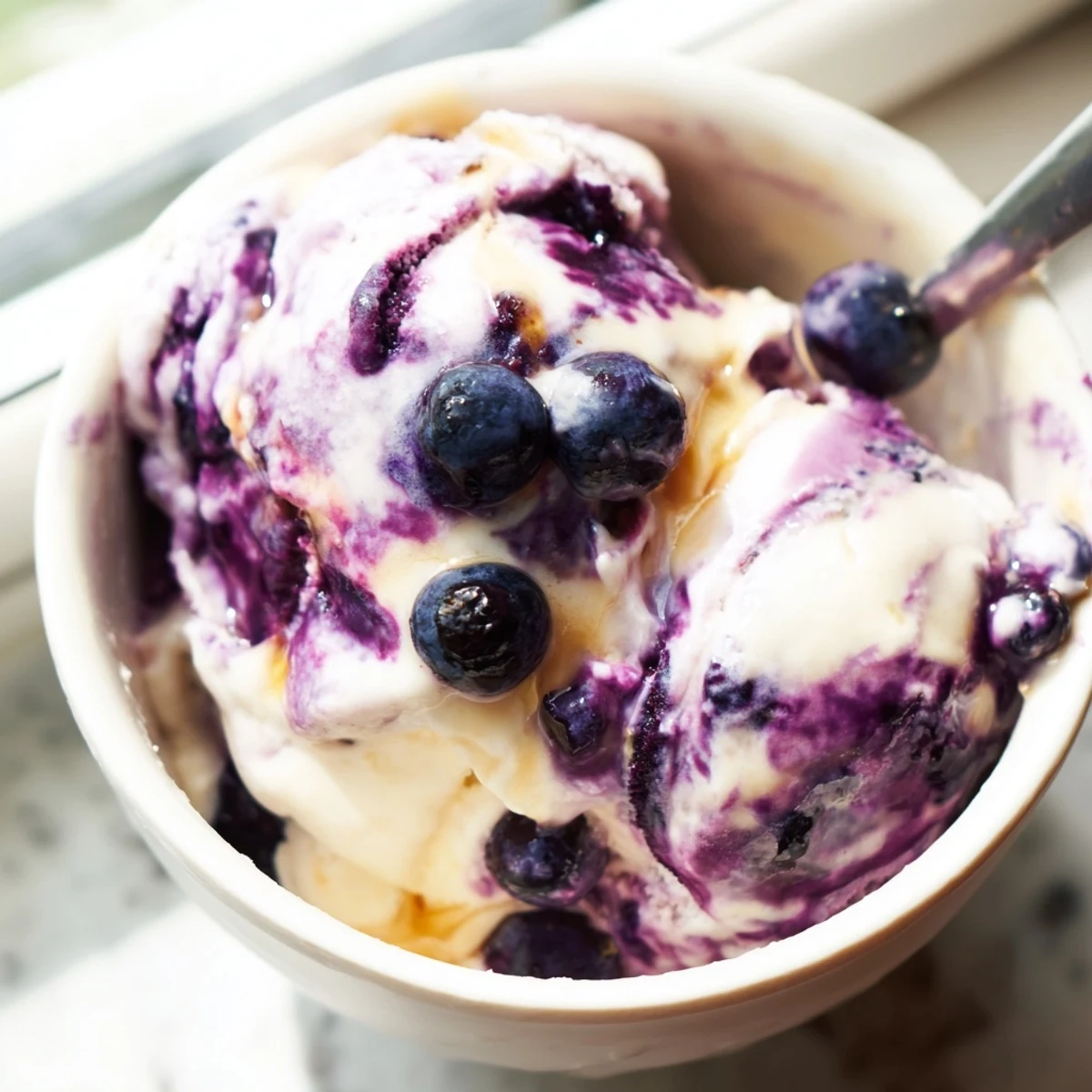 Blueberry Cottage Cheese Ice Cream scoops in a freezer container, showing a creamy, pale purple texture with visible blueberry specks.