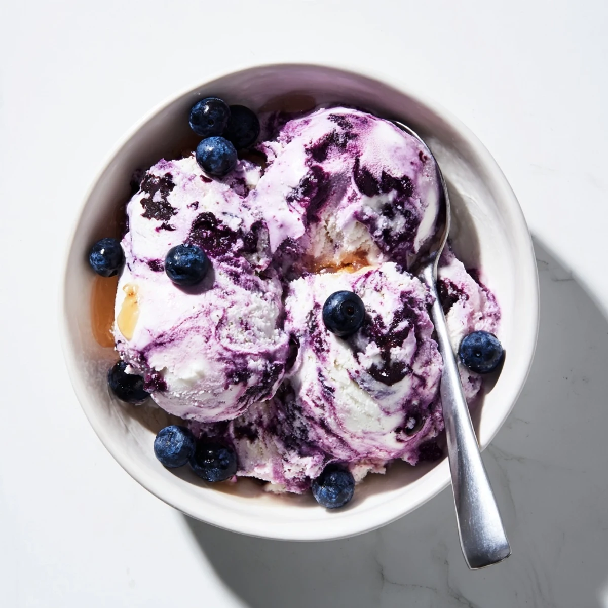 A close-up of Blueberry Cottage Cheese Ice Cream in a white bowl, topped with fresh blueberries and a drizzle of honey.