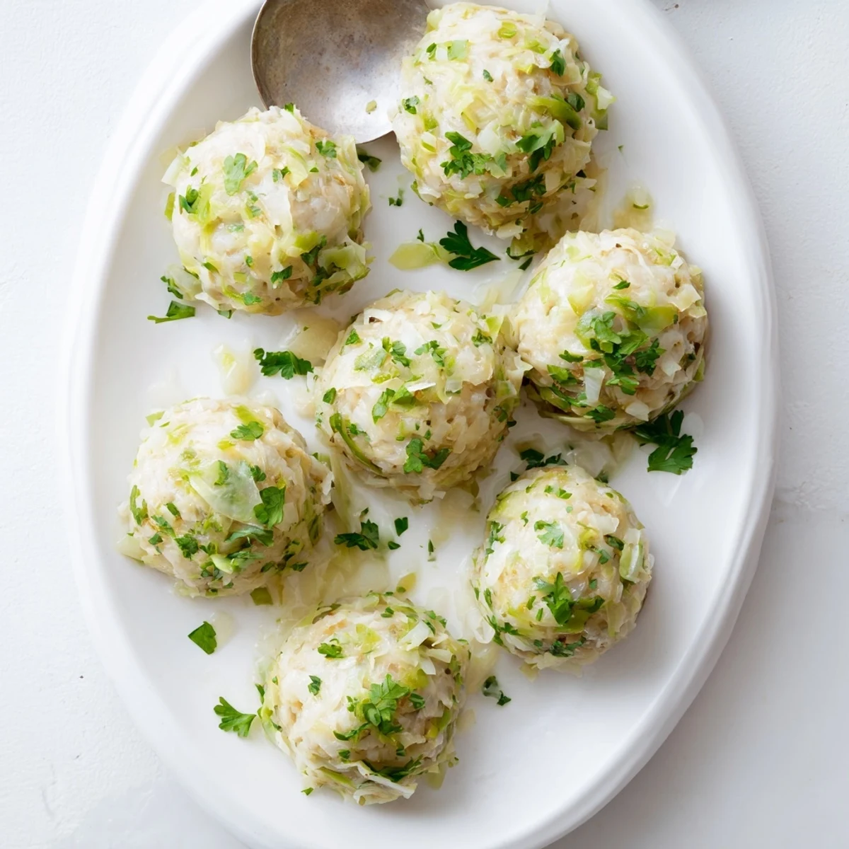 Freshly cooked German Cabbage Dumplings rest on a plate, showing their tender texture and light fluffy interior garnished with parsley.