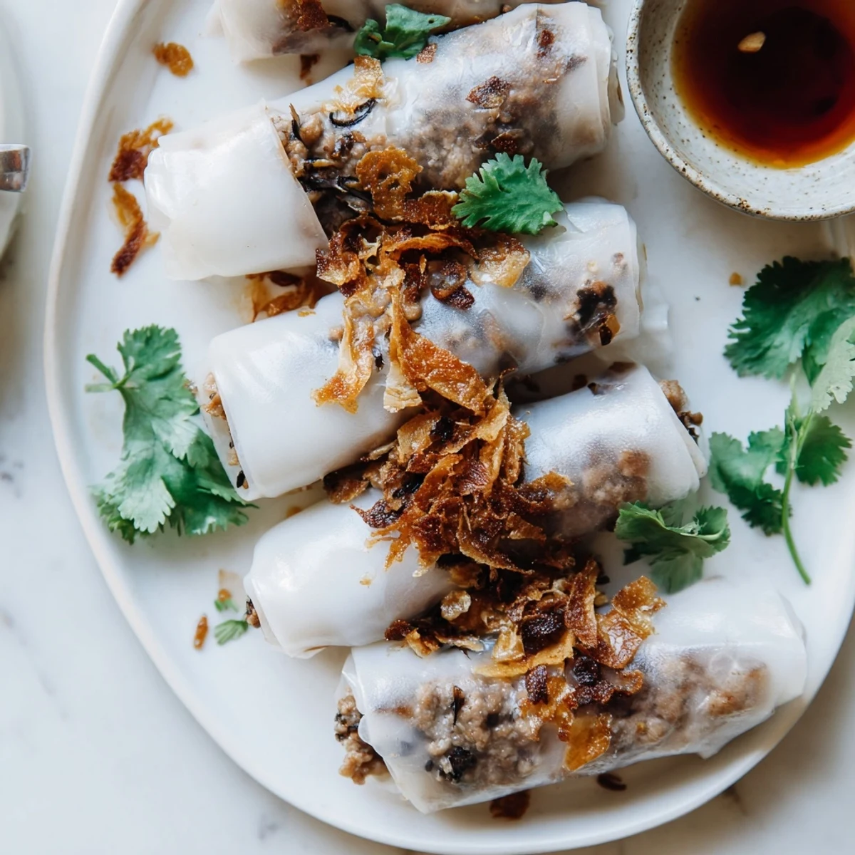 Overhead view of Banh Cuon showcasing golden fried shallots and cucumber slices next to soft translucent rice wraps for serving.