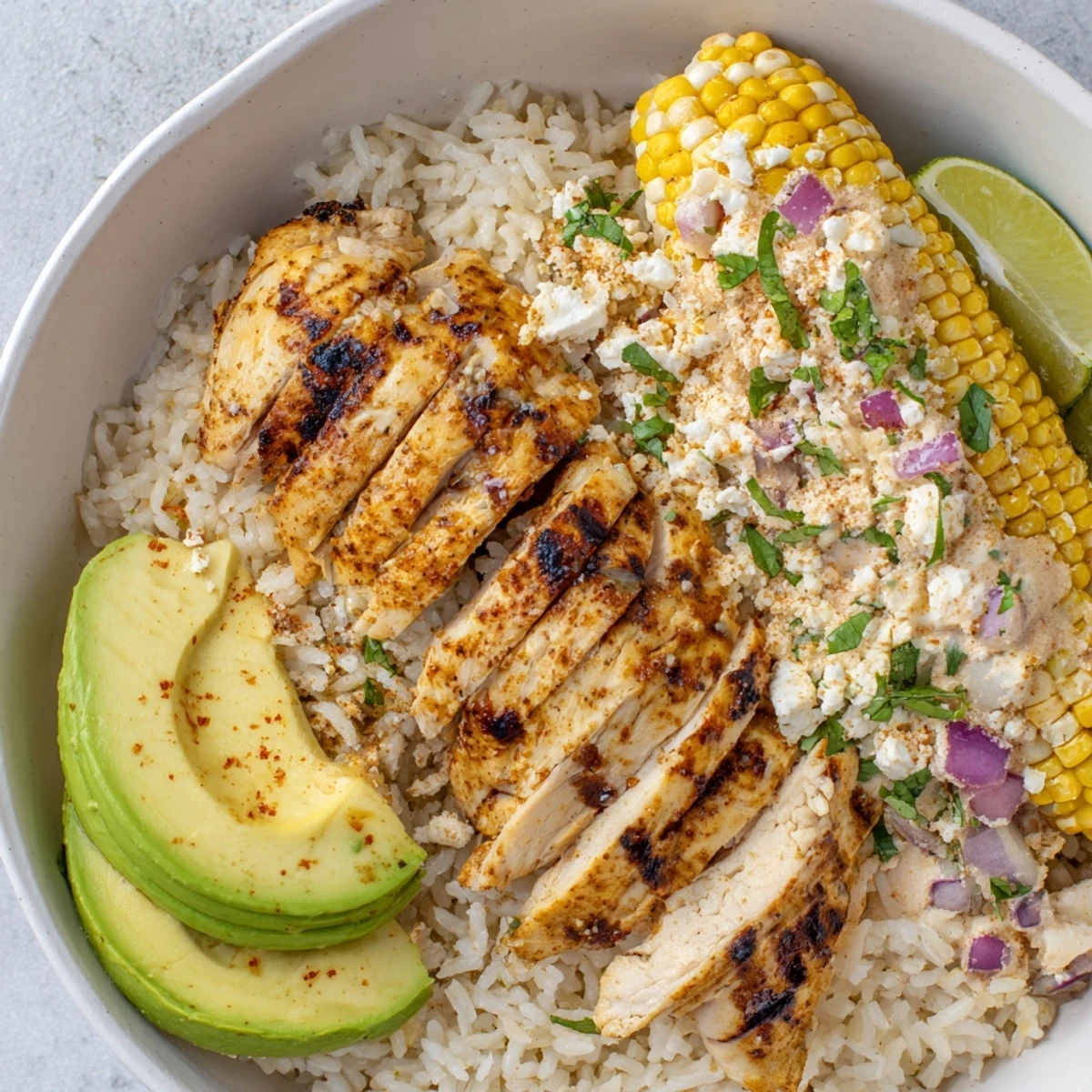 Colorful street corn chicken rice bowl featuring grilled spiced chicken over fluffy white rice topped with charred corn, creamy cotija, and fresh avocado slices