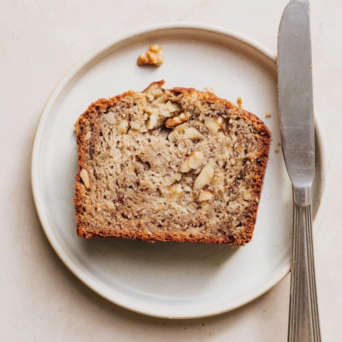 Thick slice of moist ultimate banana nut bread revealing the nutty interior texture on a white plate