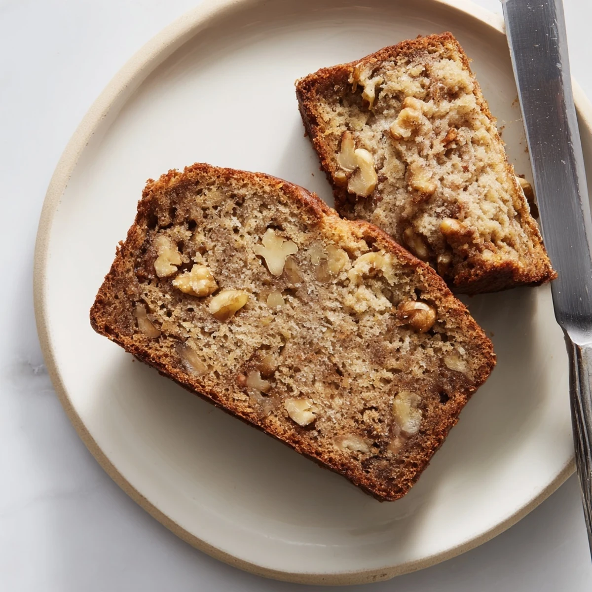Golden brown ultimate banana nut bread loaf topped with toasted walnuts on a wooden cutting board