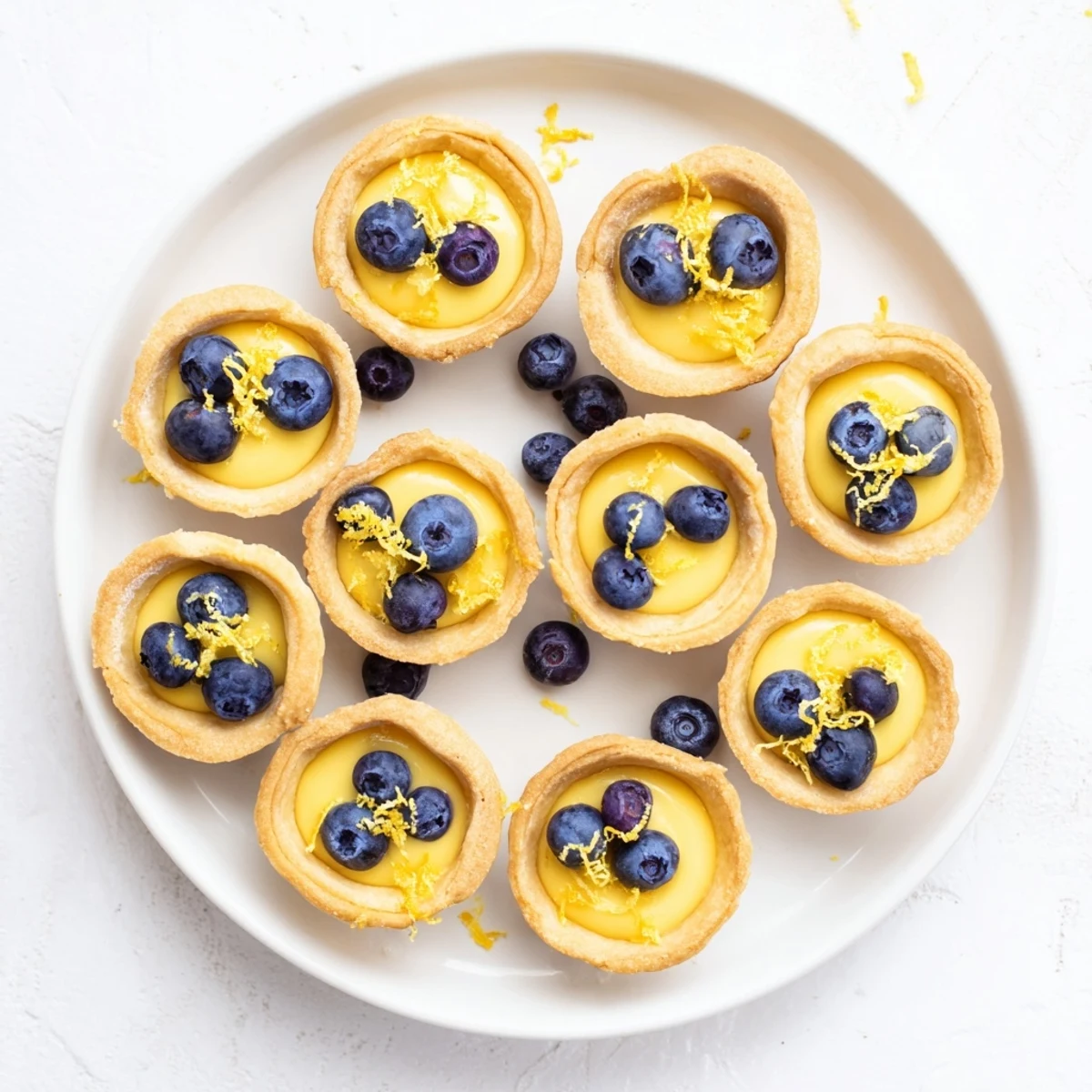 Bite-sized vegan lemon tarts topped with fresh lemon zest on a white marble serving plate