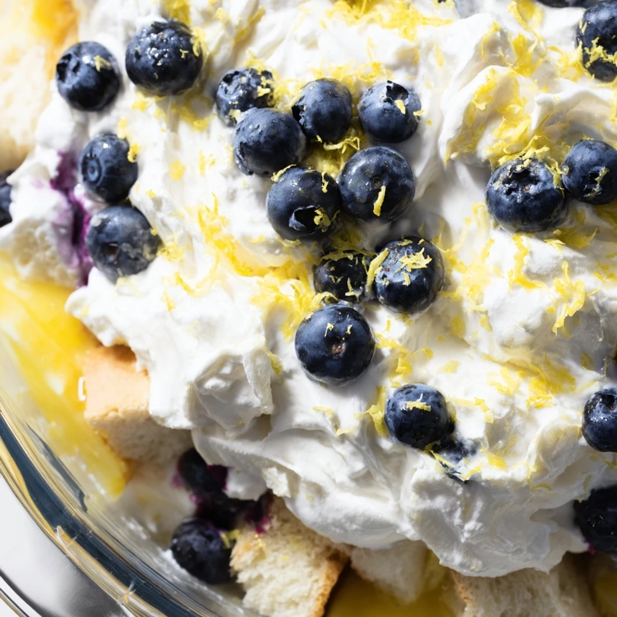 Glass bowl displaying layered lemon blueberry trifle with fresh berries and fluffy whipped cream topping