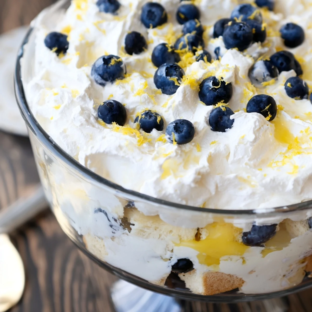 Summer dessert showing lemon blueberry trifle in clear trifle dish with zesty lemon garnish