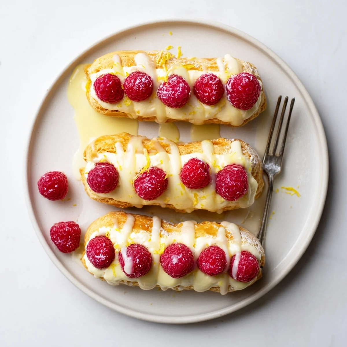 Delicate choux pastry éclairs with lemon mousse filling and bright red raspberry garnish