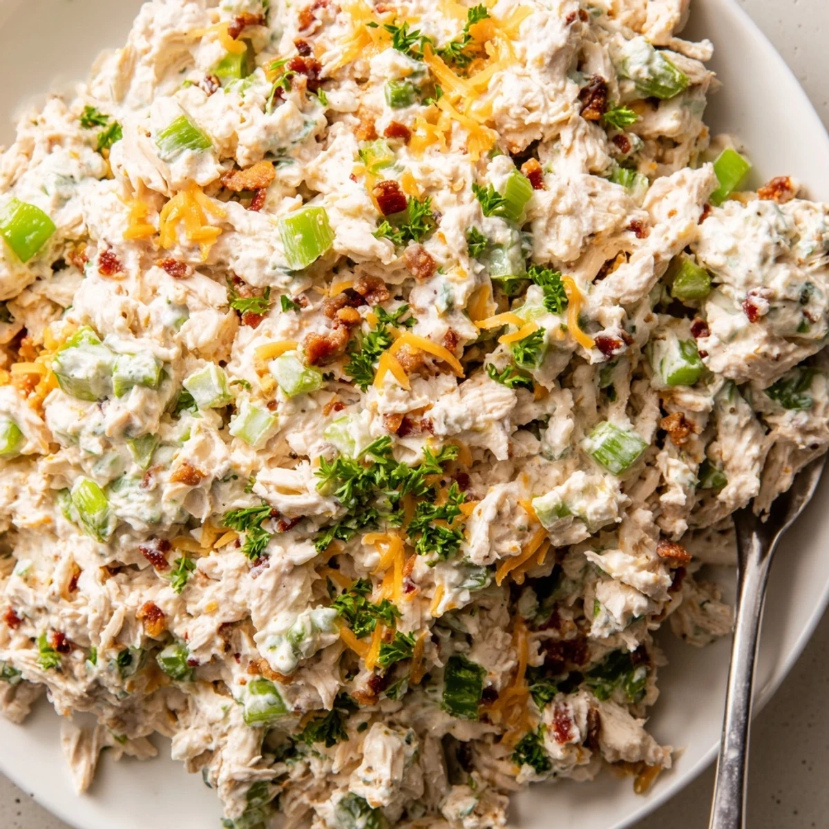 Creamy low carb jalapeno popper cottage cheese chicken salad topped with crispy bacon crumbles and fresh diced jalapeños in a white serving bowl