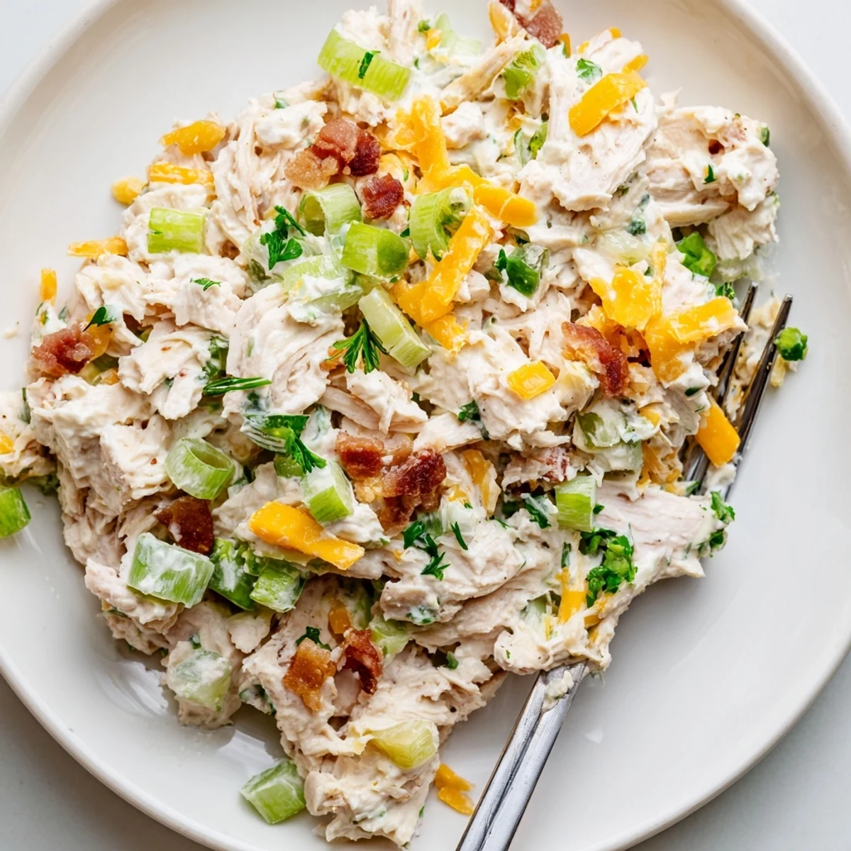 Spoonful of zesty cottage cheese chicken salad featuring melted cheddar, crunchy celery, and vibrant green onions plated on crisp lettuce leaves