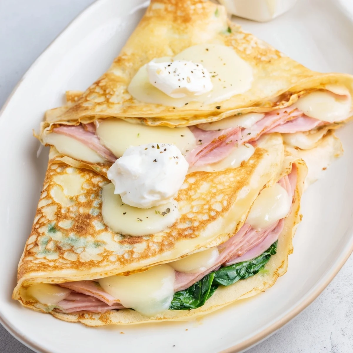 Thin savory crepes topped with ham and melted cheese, served hot on a white plate