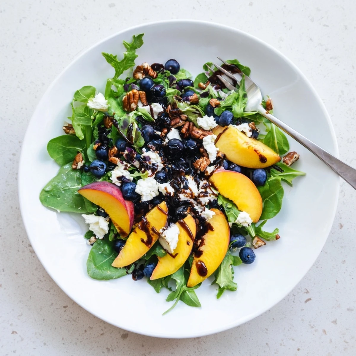 Fresh blueberry peach feta salad layered in a glass bowl with ripe peach slices