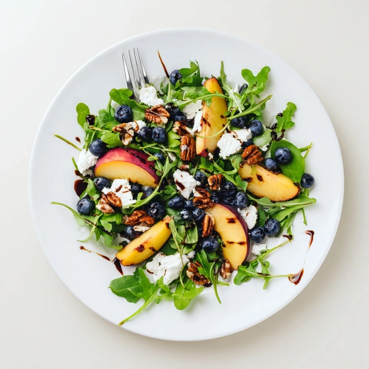Vibrant blueberry peach feta salad with toasted pecans and balsamic dressing on white plate