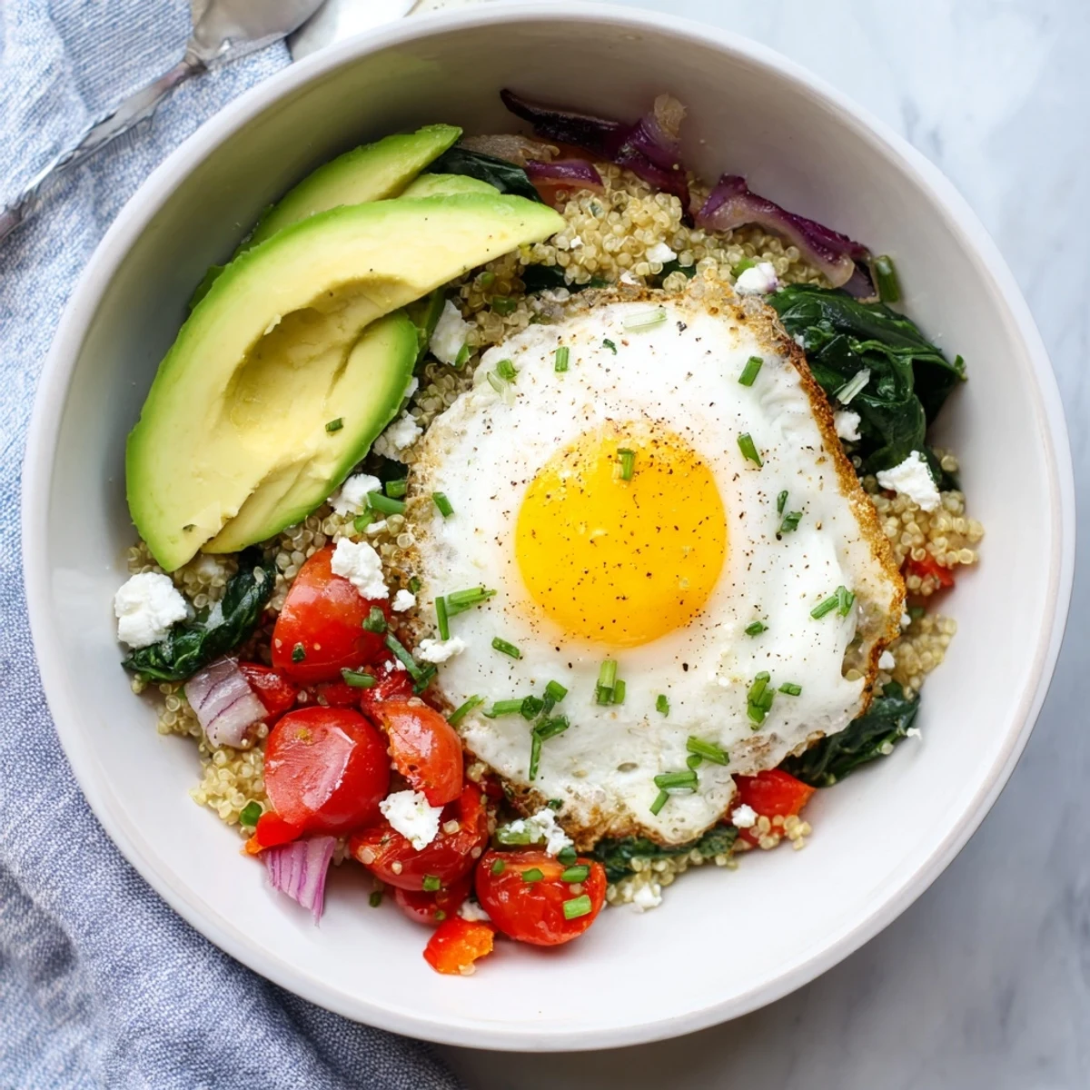 Savory quinoa breakfast bowl topped with fried egg and colorful sautéed vegetables