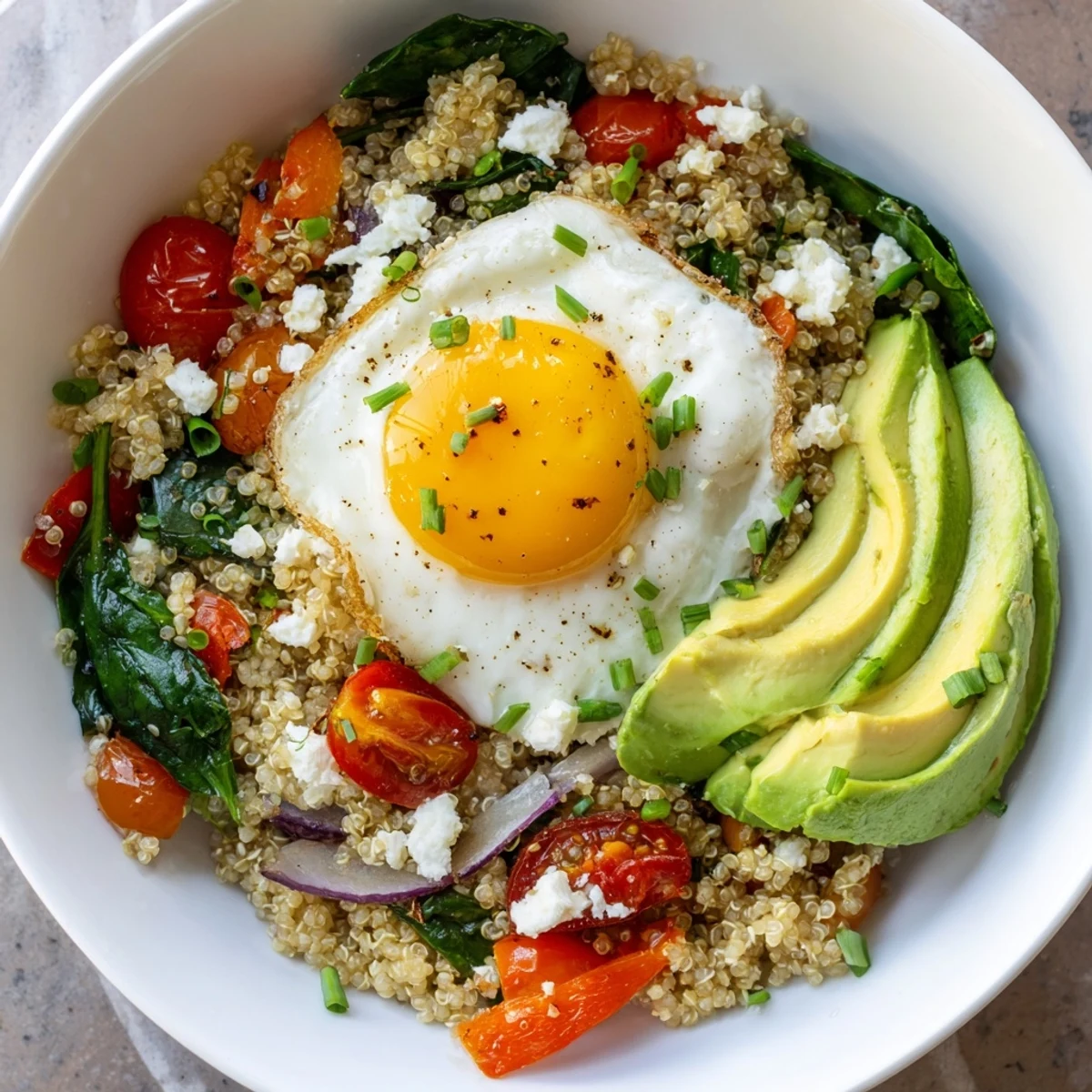 Protein-rich savory quinoa breakfast bowl with cherry tomatoes, peppers, and sunny-side-up egg