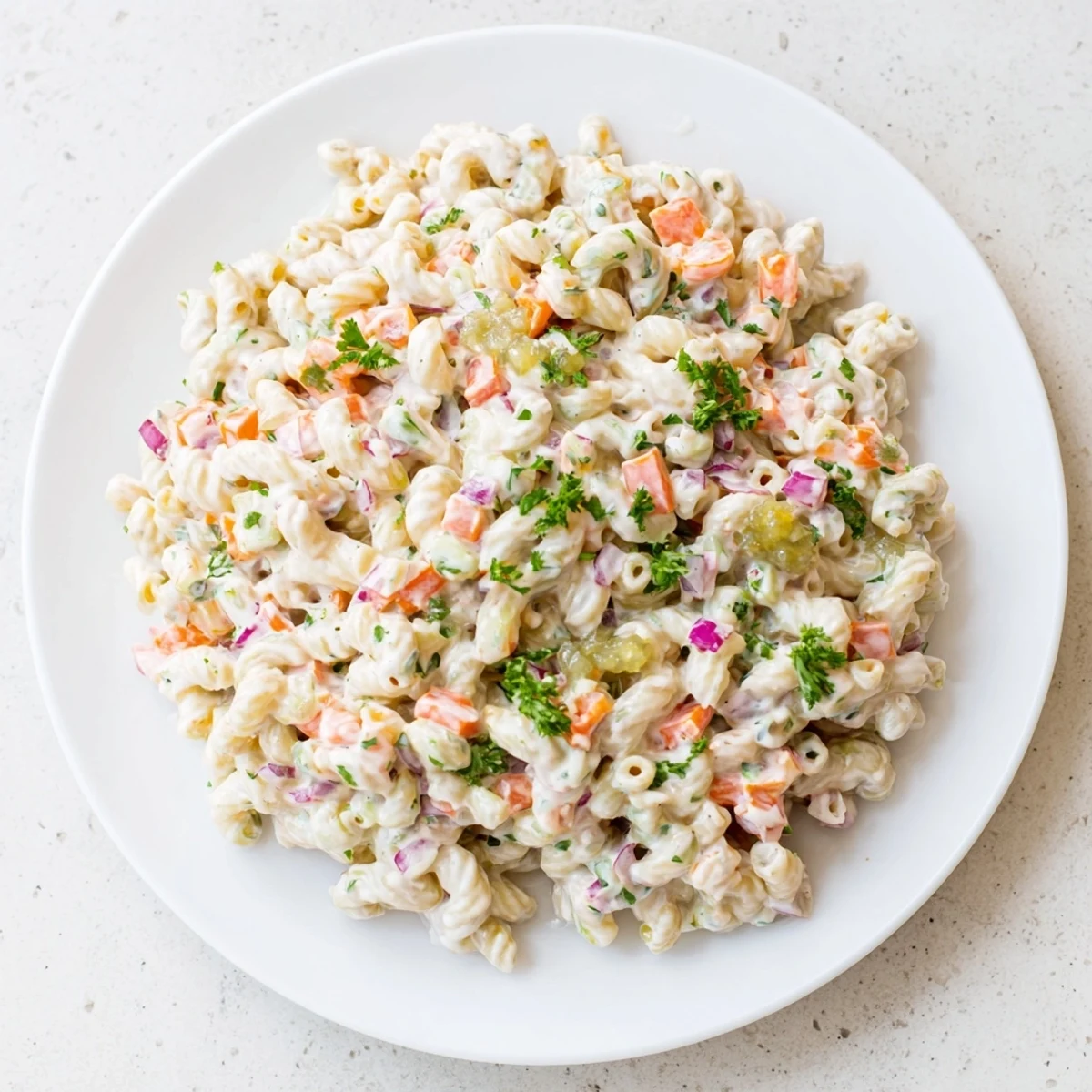 Creamy tangy macaroni salad with colorful diced vegetables in white ceramic bowl