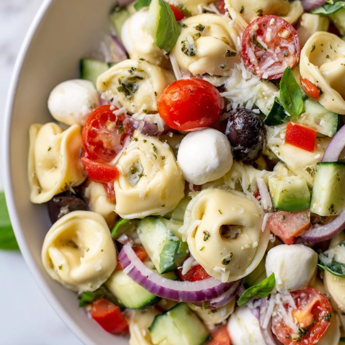 Colorful Tortellini Salad in a white bowl with cherry tomatoes, cucumber, and fresh basil leaves