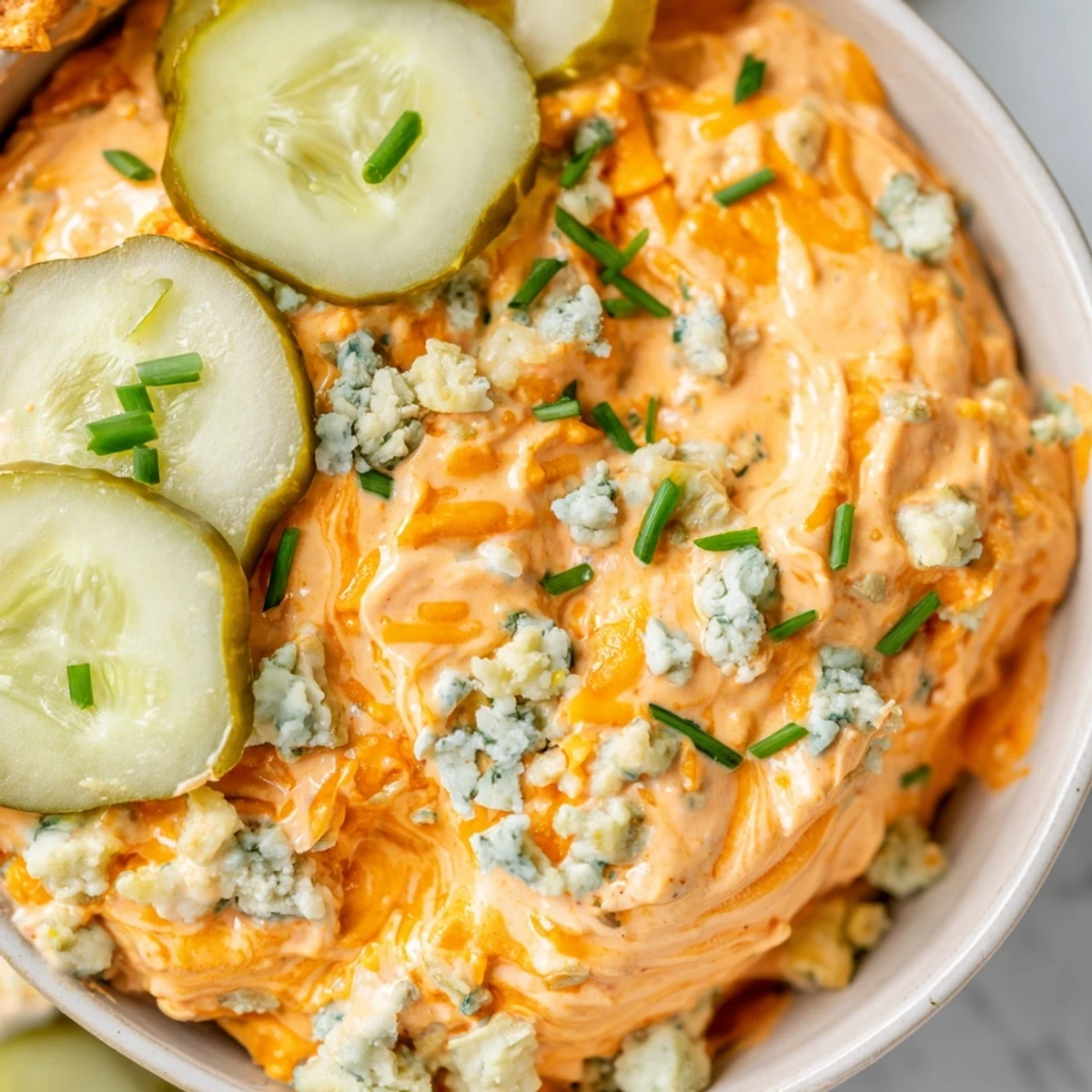Creamy buffalo pickle dip in a serving bowl surrounded by crunchy chips and fresh veggie sticks