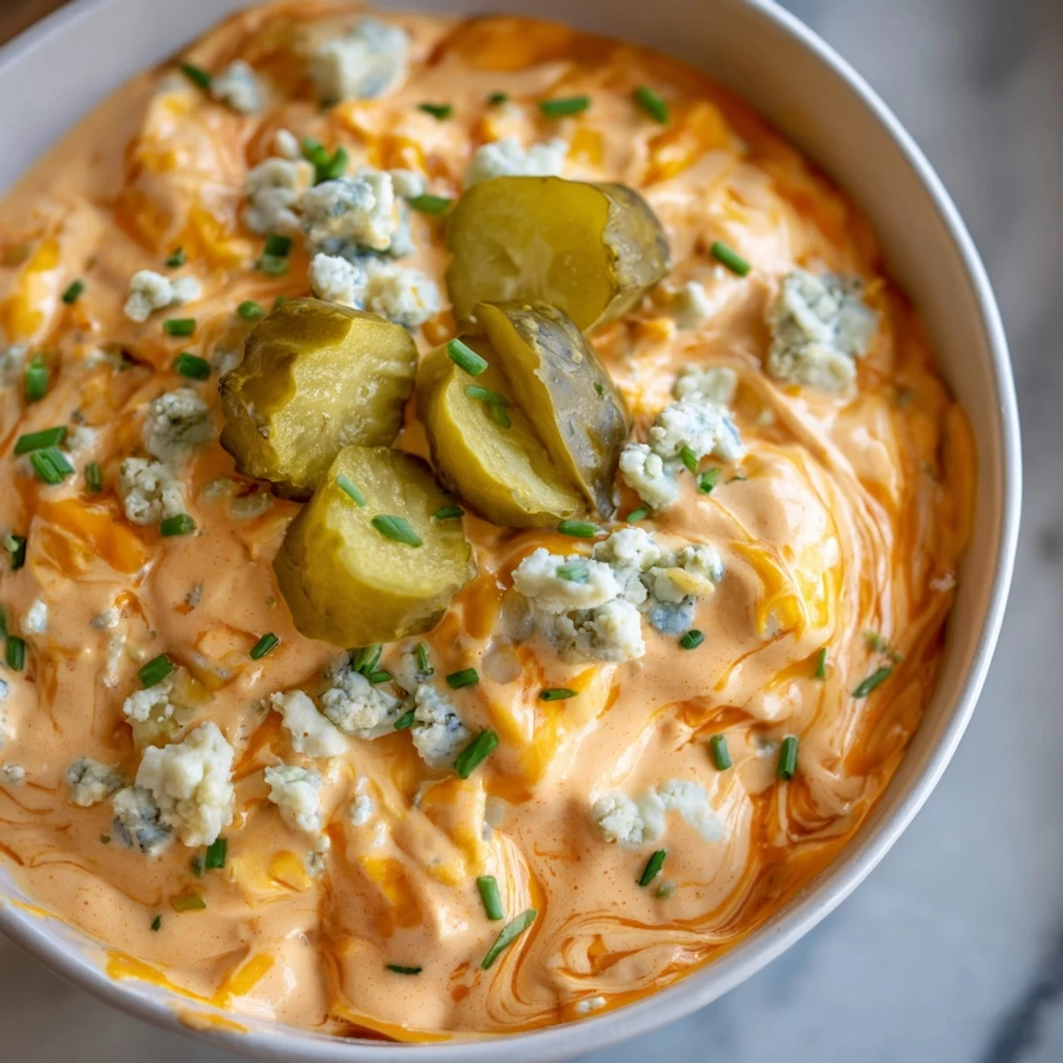 Tangy buffalo pickle dip topped with chopped chives and pickle slices on a rustic board