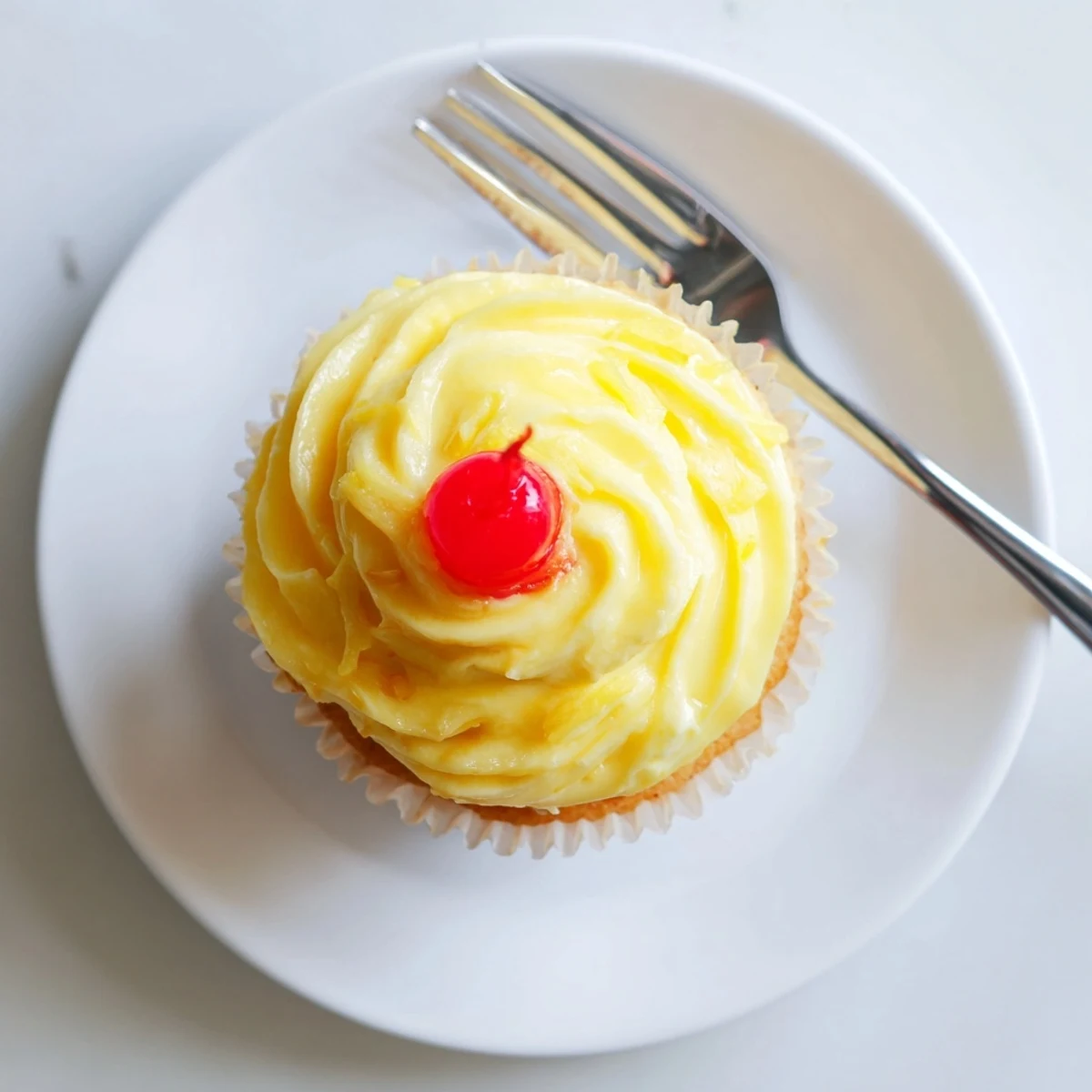 Golden Dole Whip Cupcakes topped with airy pineapple whipped frosting and a cherry garnish
