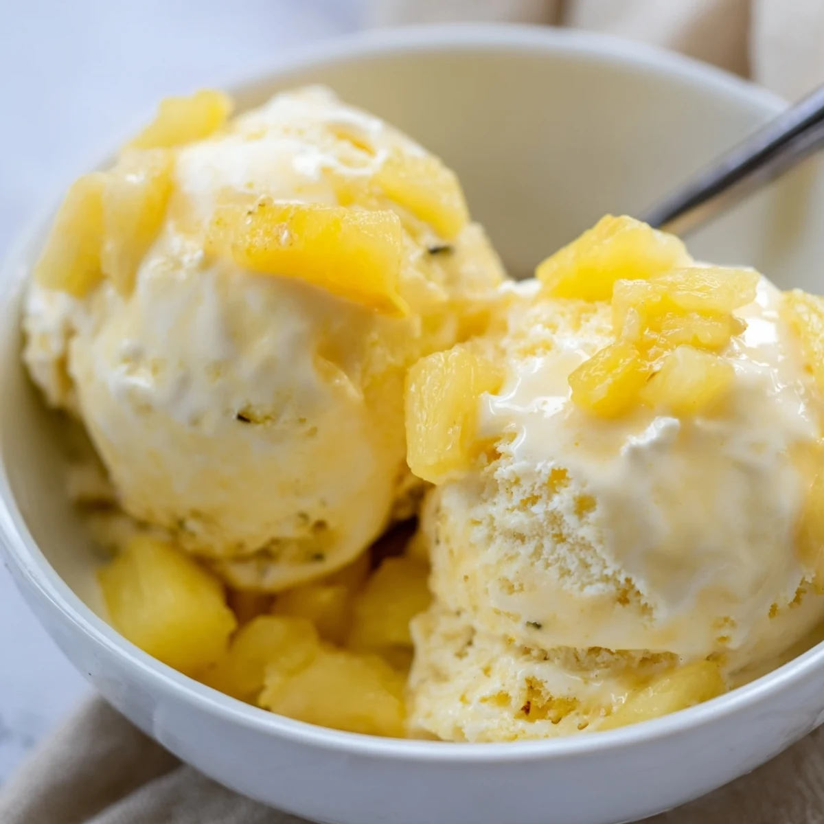 Homemade Creamy Pineapple Ice Cream garnished with toasted coconut and a spoon.  