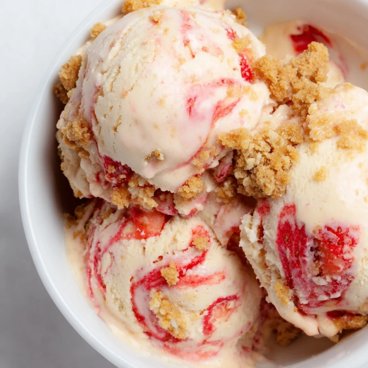 Scoop of velvety strawberry cheesecake ice cream marbled with sweet strawberry sauce and crispy graham cracker pieces