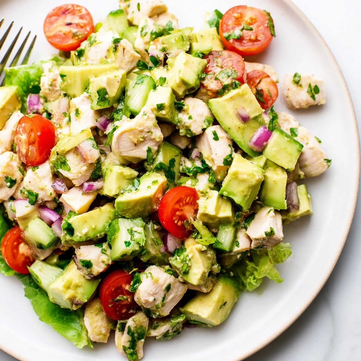 Bright Avocado Chicken Salad with cherry tomatoes, red onion, cilantro garnish.