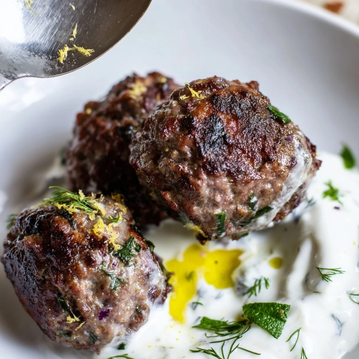 Greek Style Beef Meatballs glistening with olive oil, served with creamy yogurt.