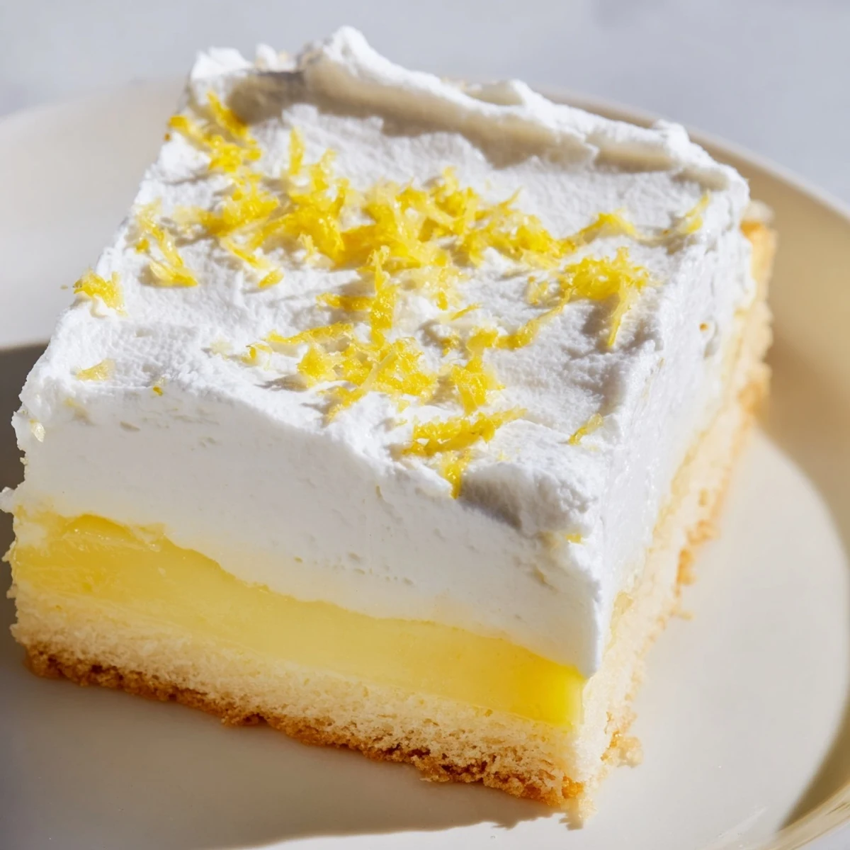 Layered lemon lush cake dessert with whipped topping and fresh lemon zest garnish on white plate