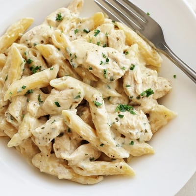 In a slow cooker, tender Crockpot Garlic Parmesan Chicken Pasta is stirred in a crockpot, steam rising from a rich, garlicky sauce.