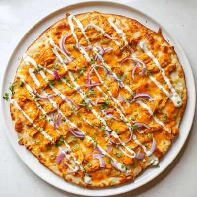 Close-up of Bold Buffalo Chicken Pizza with red onion and scallions, drizzled with ranch and extra buffalo sauce.
