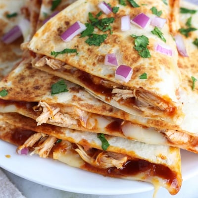 Sizzling Hot Honey BBQ Chicken Quesadillas in a skillet with diced red onion and fresh cilantro garnish.