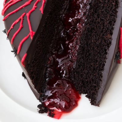 A glossy black cocoa ganache drips down this spooky Black Widow Cake decorated with red vein piping and edible spiders