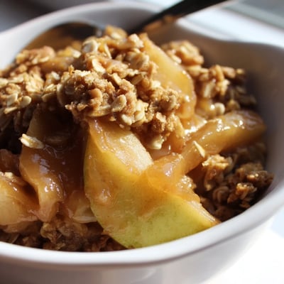 Crockpot Apple Crisp scooped into a bowl with melting vanilla ice cream on top